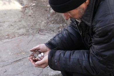 Poor homeless man holding coins outdoors, closeup