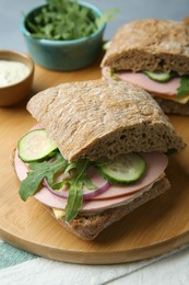 Photo of Tasty sandwiches with boiled sausage, cucumber, arugula and sauce on table, closeup