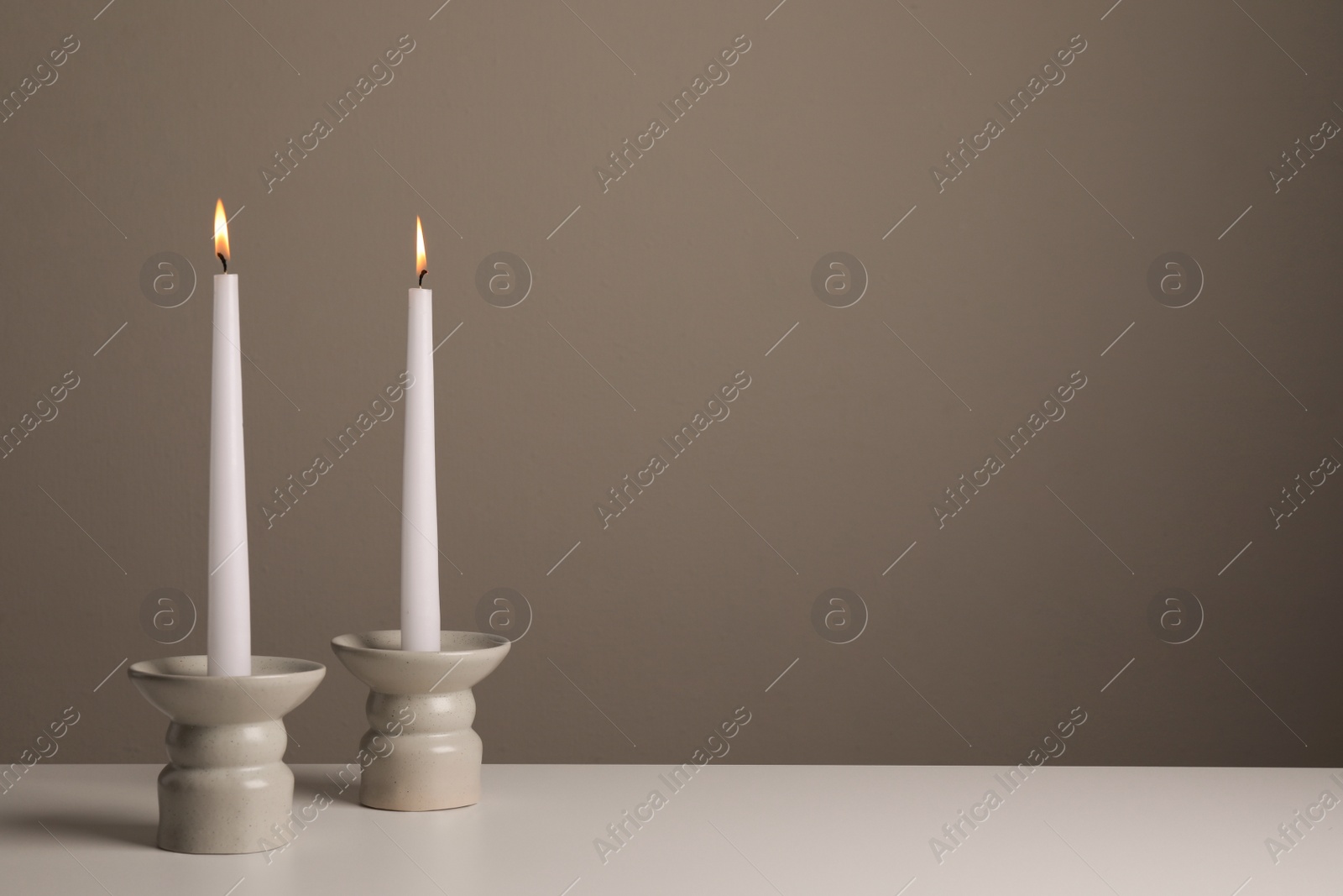 Photo of Holders with burning candles on white table near pale brown wall, space for text