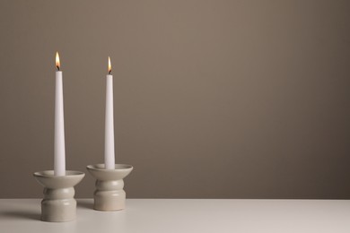 Photo of Holders with burning candles on white table near pale brown wall, space for text