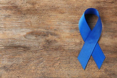 Blue awareness ribbon on wooden background, top view with space for text. Symbol of social and medical issues