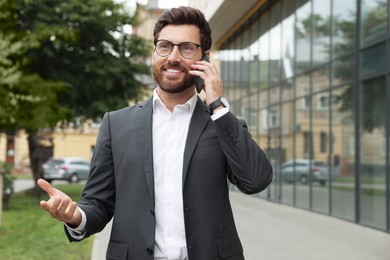 Photo of Handsome businessman talking on smartphone while walking outdoors