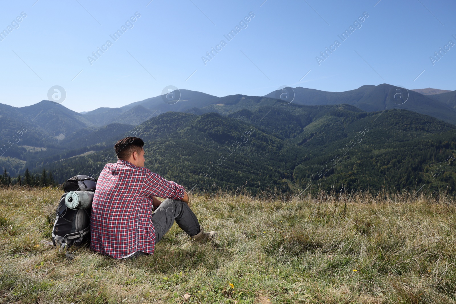 Photo of Tourist with backpack sitting on ground and enjoying landscape in mountains, back view