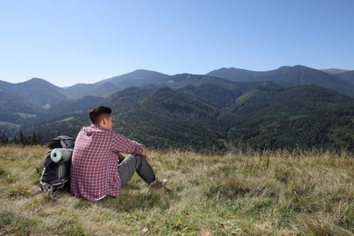 Photo of Tourist with backpack sitting on ground and enjoying landscape in mountains, back view