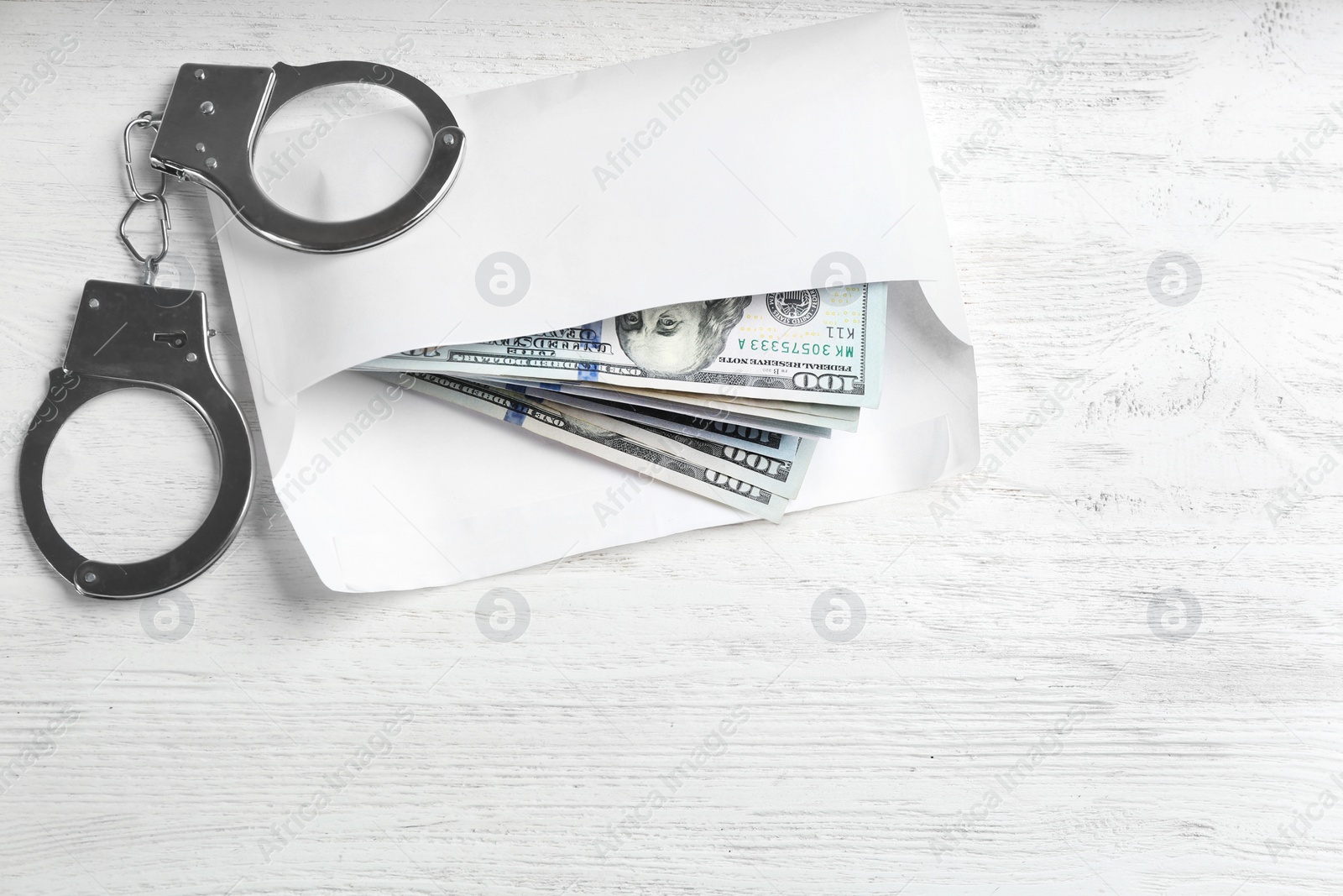 Photo of Dollar bills and handcuffs on white wooden table, flat lay. Bribe concept