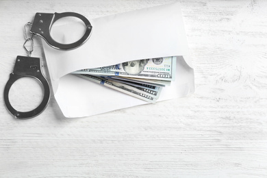 Photo of Dollar bills and handcuffs on white wooden table, flat lay. Bribe concept