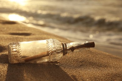 Photo of SOS message in glass bottle on sand near sea