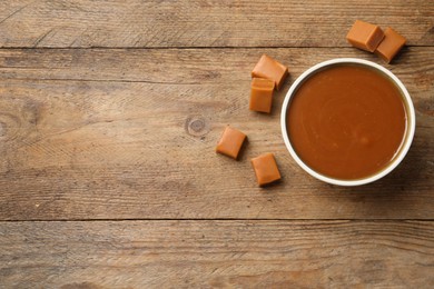 Yummy salted caramel in bowl and candies on wooden table, flat lay. Space for text