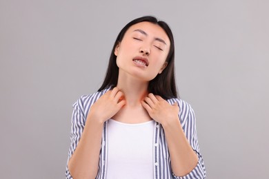 Suffering from allergy. Young woman scratching her neck on grey background