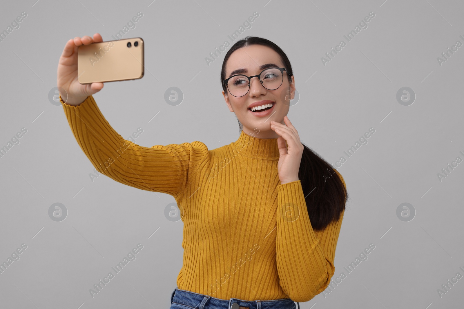 Photo of Smiling young woman taking selfie with smartphone on grey background