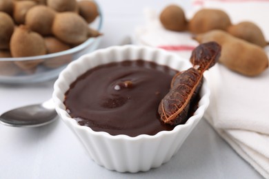 Photo of Bowl of tamarind sauce and fresh pods on light table, closeup