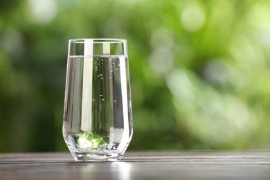 Glass of fresh water on wooden table outdoors. Space for text
