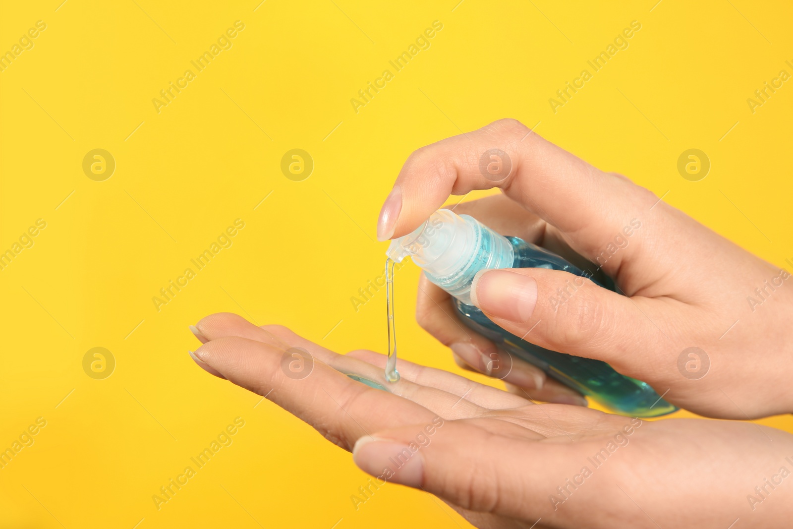 Photo of Woman applying antiseptic gel on yellow background, closeup