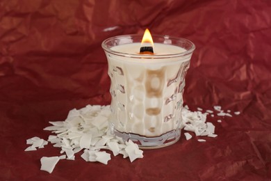 Burning soy candle and wax flakes on crumpled red paper