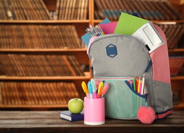 Backpack with school stationery on wooden table in library, space for text