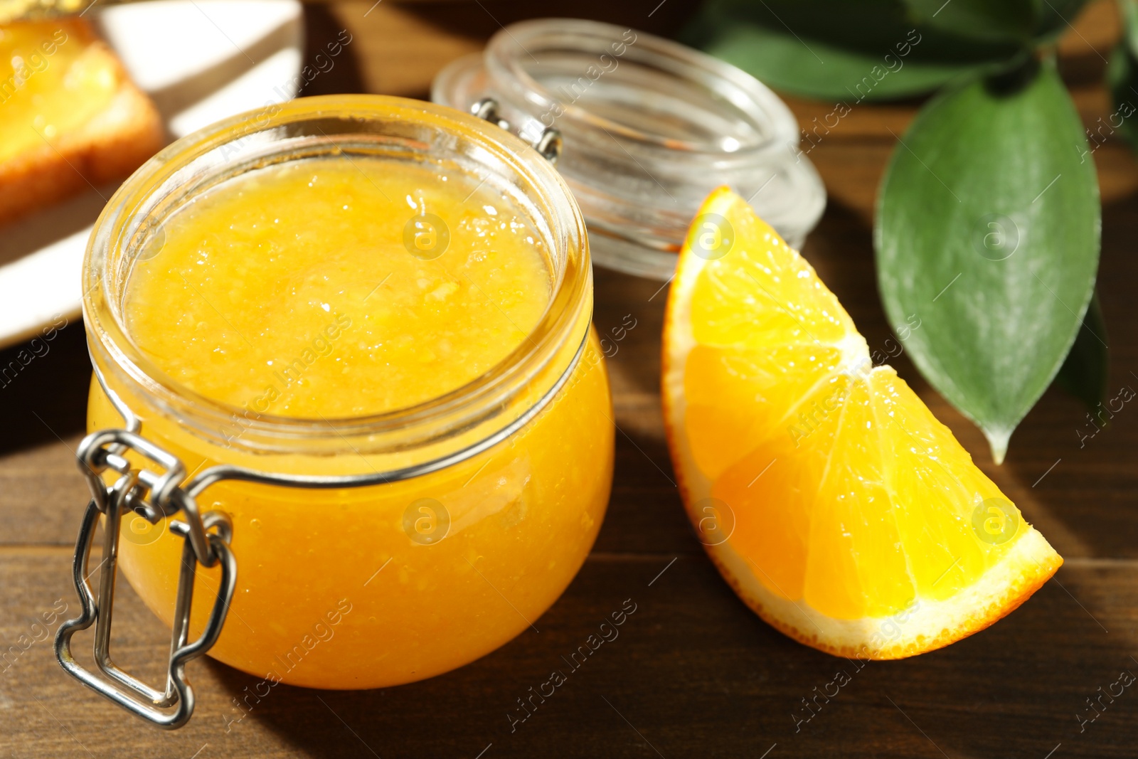 Photo of Delicious orange marmalade and citrus fruit slice on wooden table, closeup