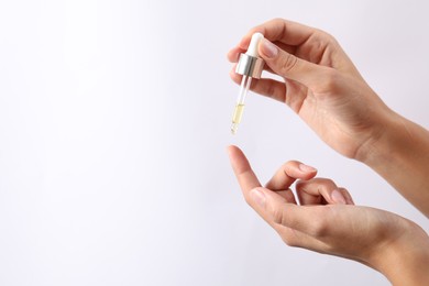 Photo of Woman applying cosmetic serum onto her finger on white background, closeup. Space for text