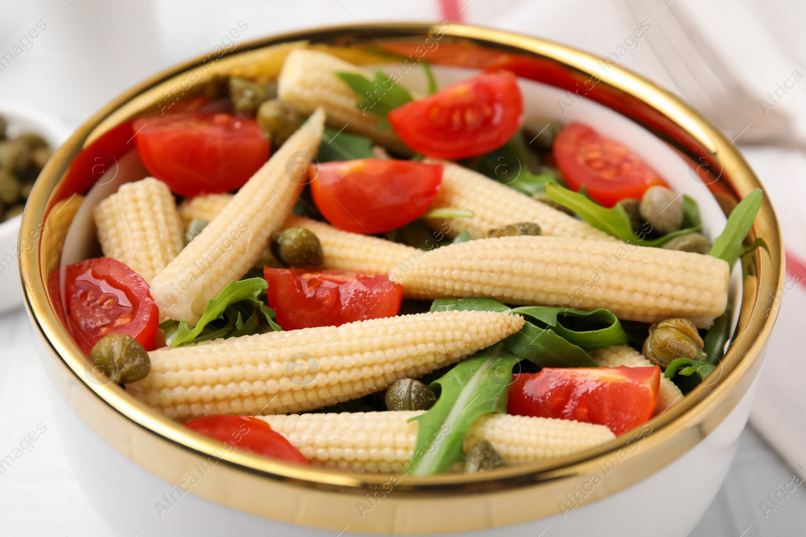 Photo of Tasty baby corn with tomatoes, arugula and capers on white table, closeup