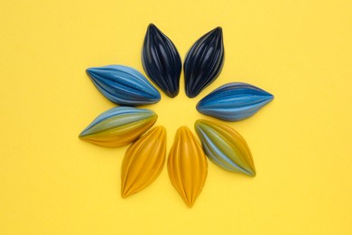Photo of Tasty chocolate candies in shape of flower on yellow background, top view