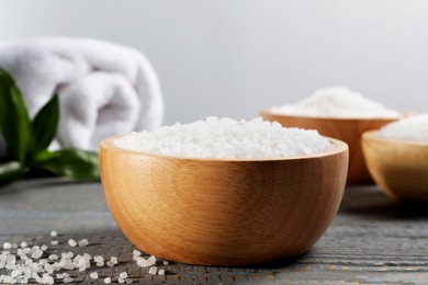 Bowls of natural sea salt on grey wooden table, closeup