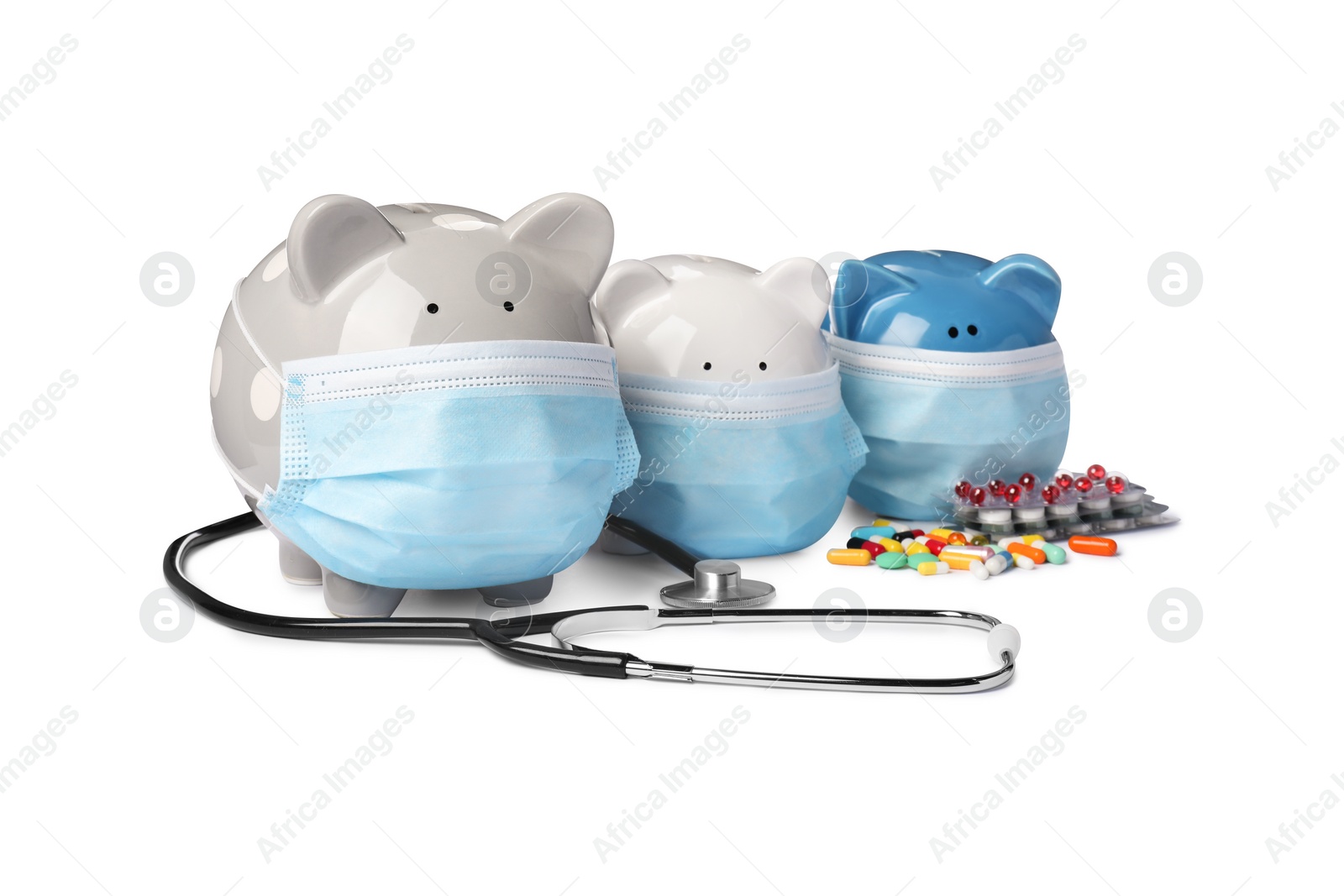 Photo of Piggy banks in protective masks, stethoscope and pills on white background. Medical insurance