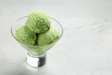 Photo of Delicious green ice cream served in dessert bowl on white wooden table. Space for text