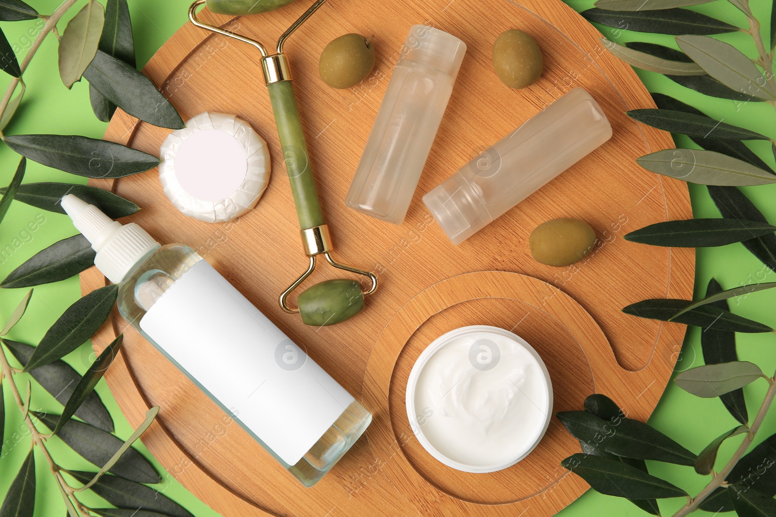 Photo of Different cosmetic products, face roller and olives on light green background, flat lay