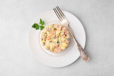 Photo of Tasty Olivier salad with boiled sausage and fork on light table, top view