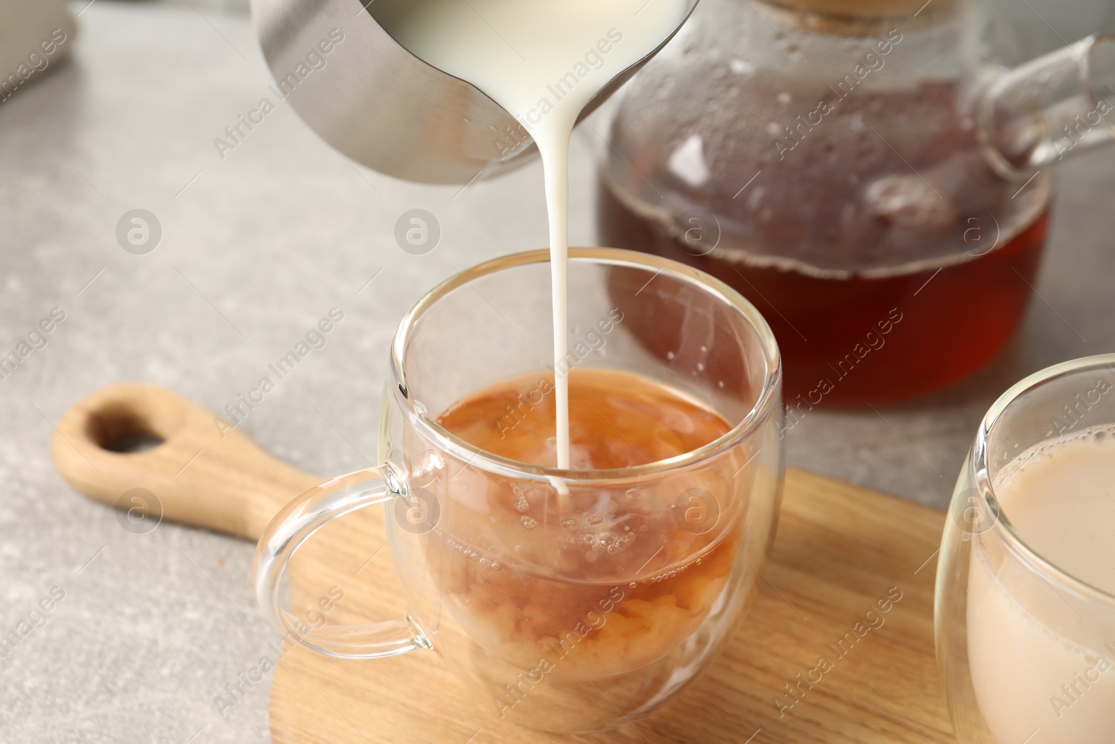 Photo of Pouring milk into glass cup with tea at light grey table, closeup