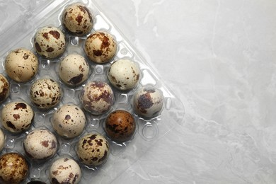 Photo of Plastic container with speckled quail eggs on light grey marble table, top view. Space for text