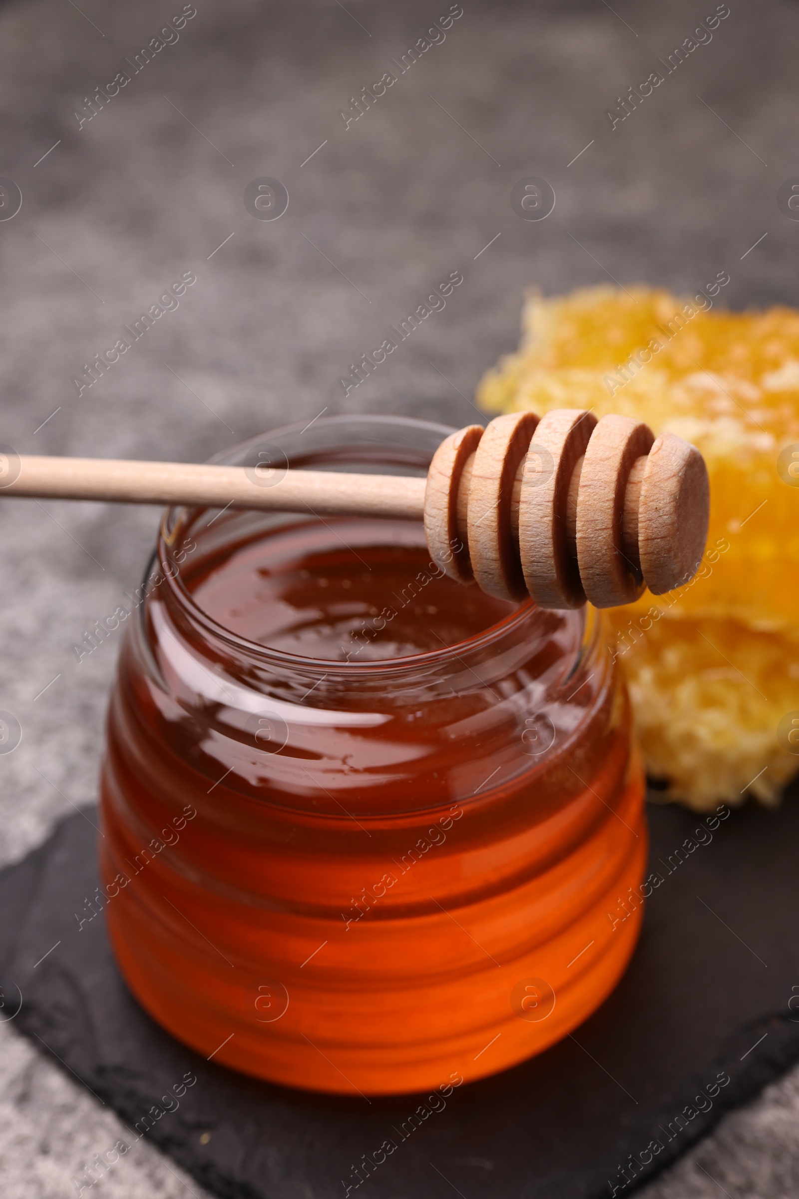 Photo of Sweet golden honey in jar and dipper on grey table, closeup