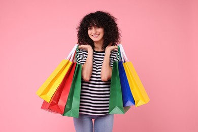 Happy young woman with shopping bags on pink background