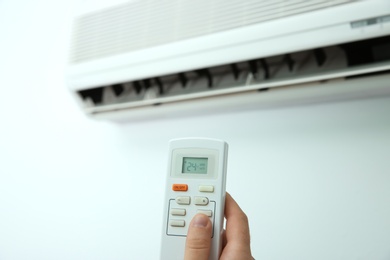 Photo of Man operating air conditioner with remote control indoors