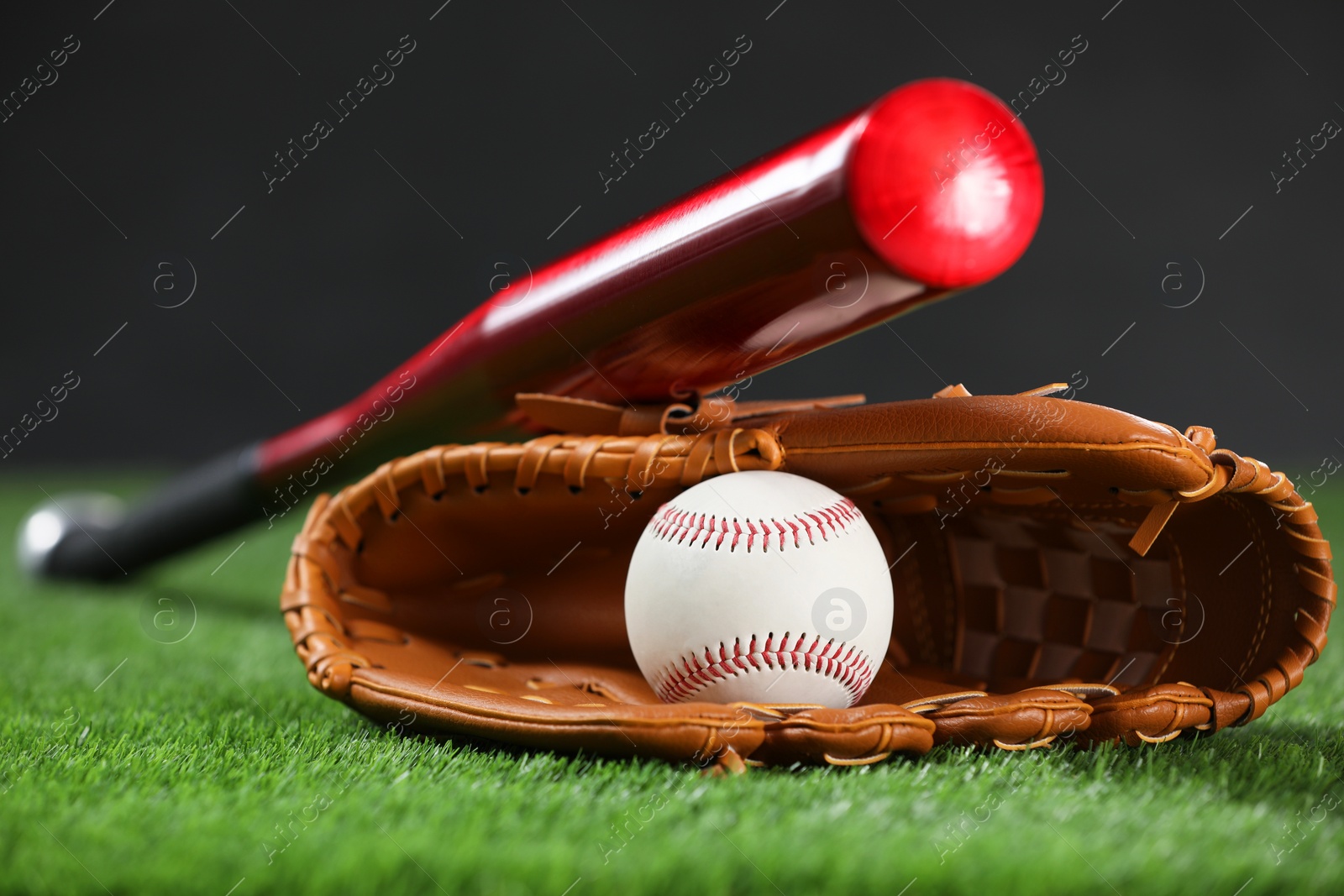 Photo of Baseball bat, leather glove and ball on green grass against dark background, closeup