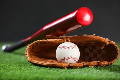 Baseball bat, leather glove and ball on green grass against dark background, closeup