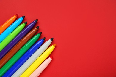Photo of Different colorful markers on red background, flat lay. Space for text