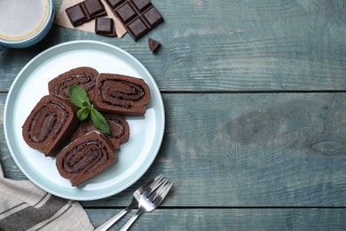 Photo of Tasty chocolate cake roll with cream and mint on blue wooden table, flat lay. Space for text