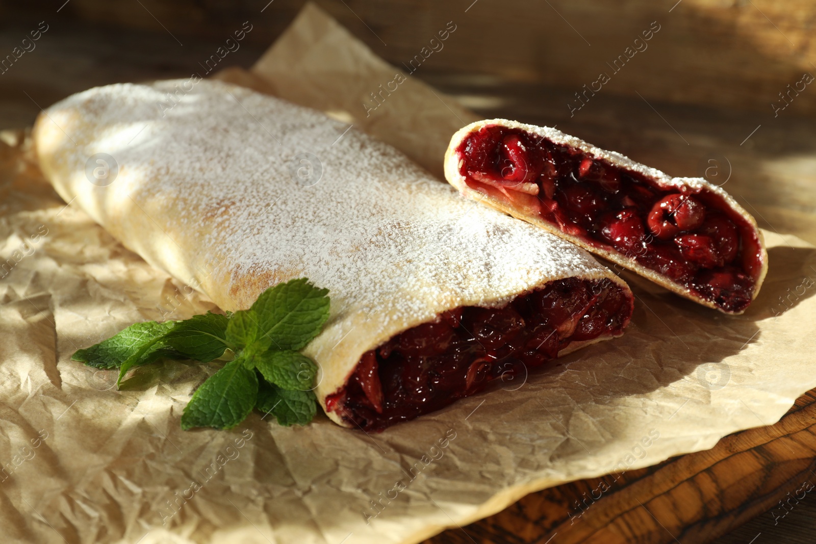 Photo of Delicious strudel with cherries, powdered sugar and mint on board, closeup