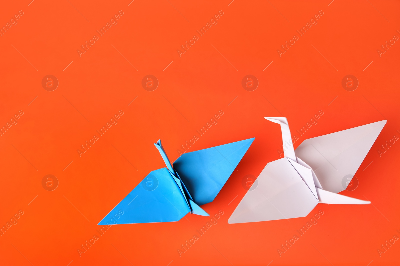 Photo of Colorful paper origami cranes on orange background, flat lay. Space for text