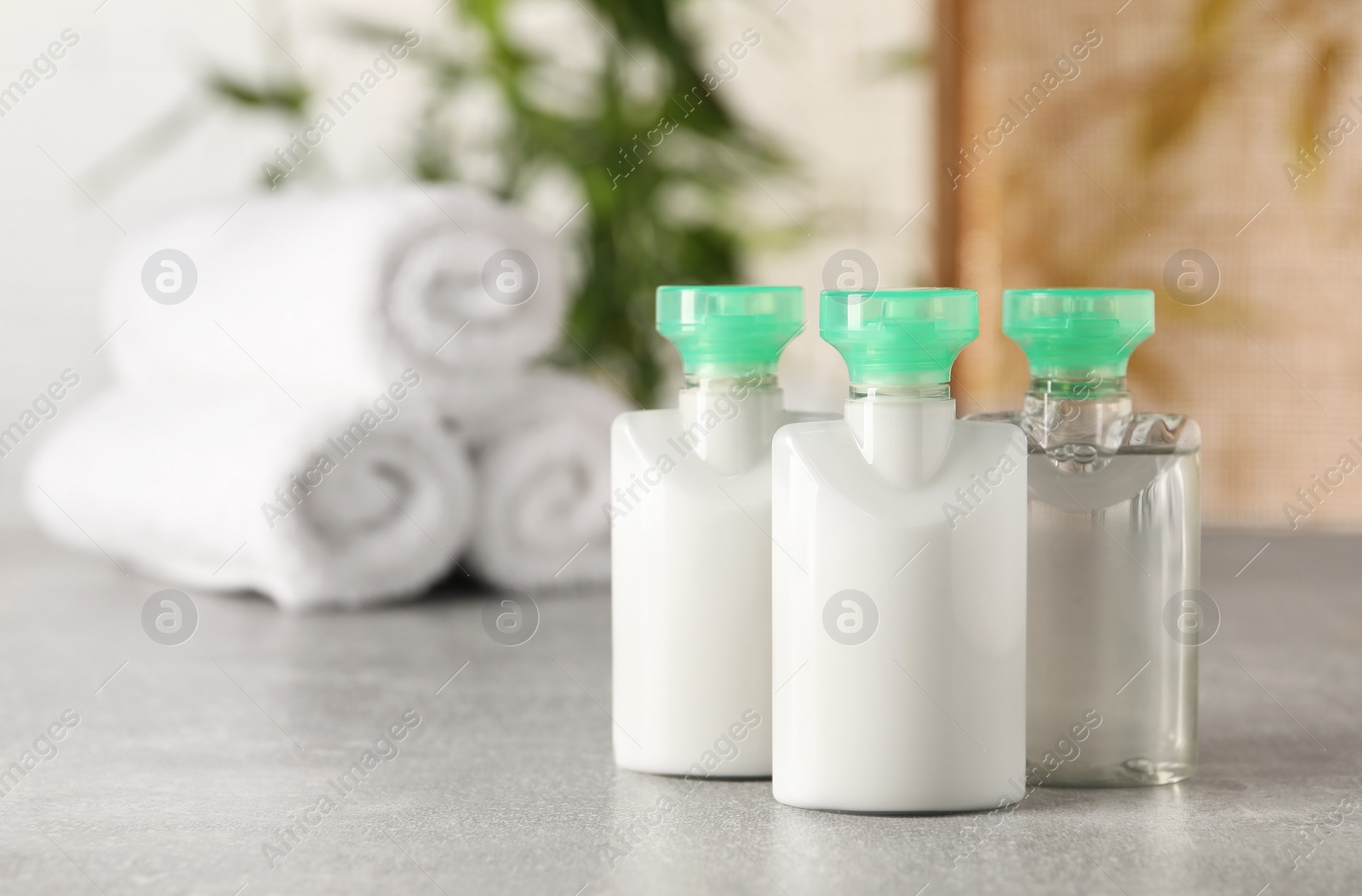 Photo of Mini bottles of cosmetic products on light grey table against blurred background. Space for text