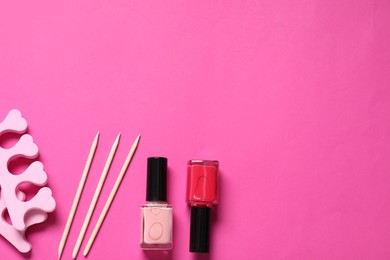 Photo of Nail polishes, orange sticks and toe separators on pink background, flat lay. Space for text
