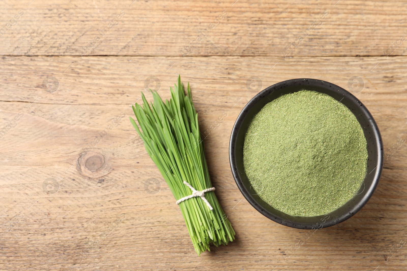 Photo of Wheat grass powder in bowl and fresh green sprouts on wooden table, flat lay. Space for text