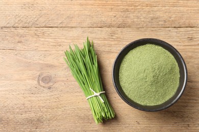 Wheat grass powder in bowl and fresh green sprouts on wooden table, flat lay. Space for text