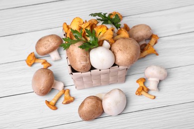 Basket with different mushrooms and parsley on white wooden table