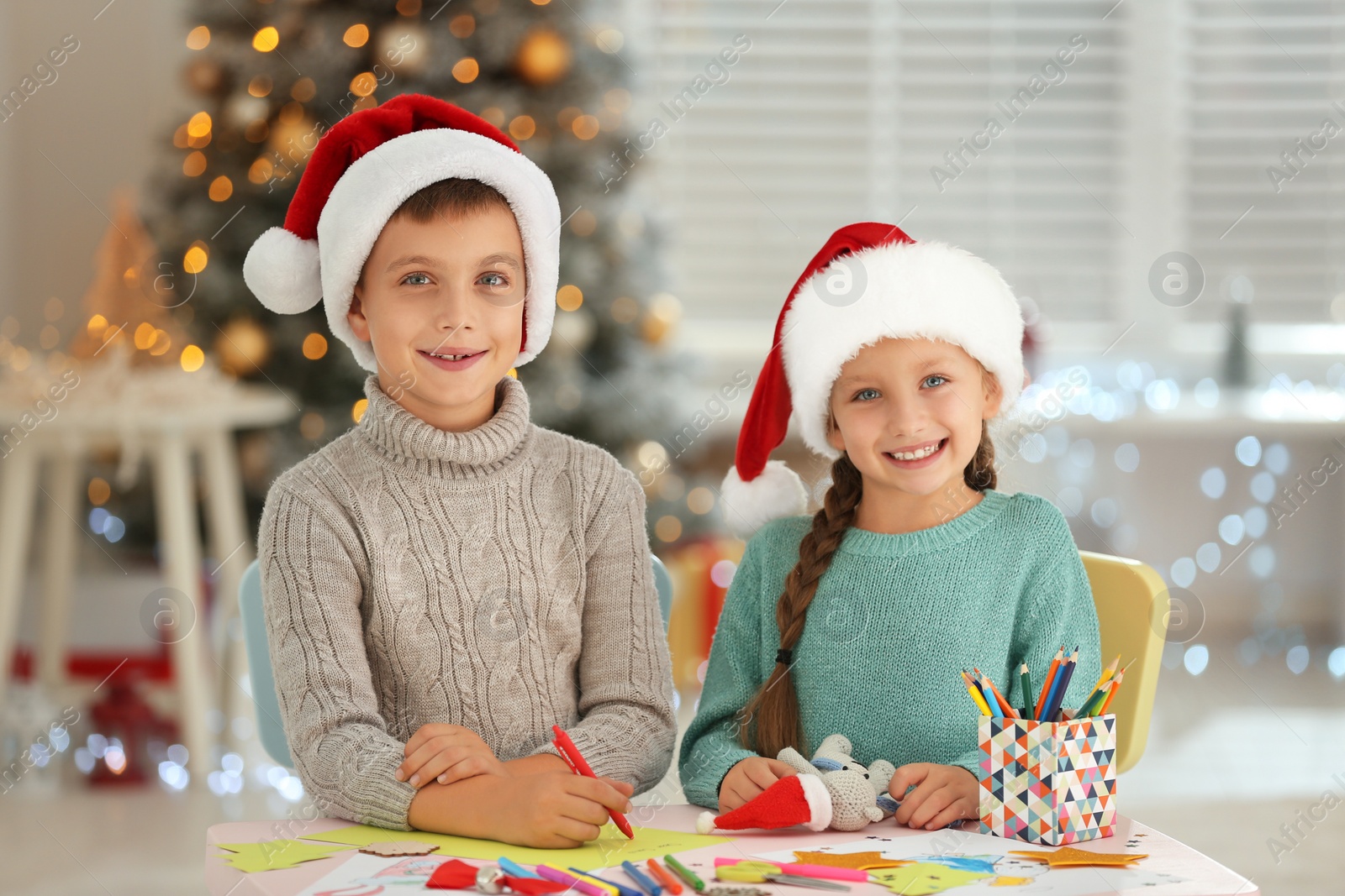 Photo of Little children in Santa hats making craftworks at table indoors. Christmas season