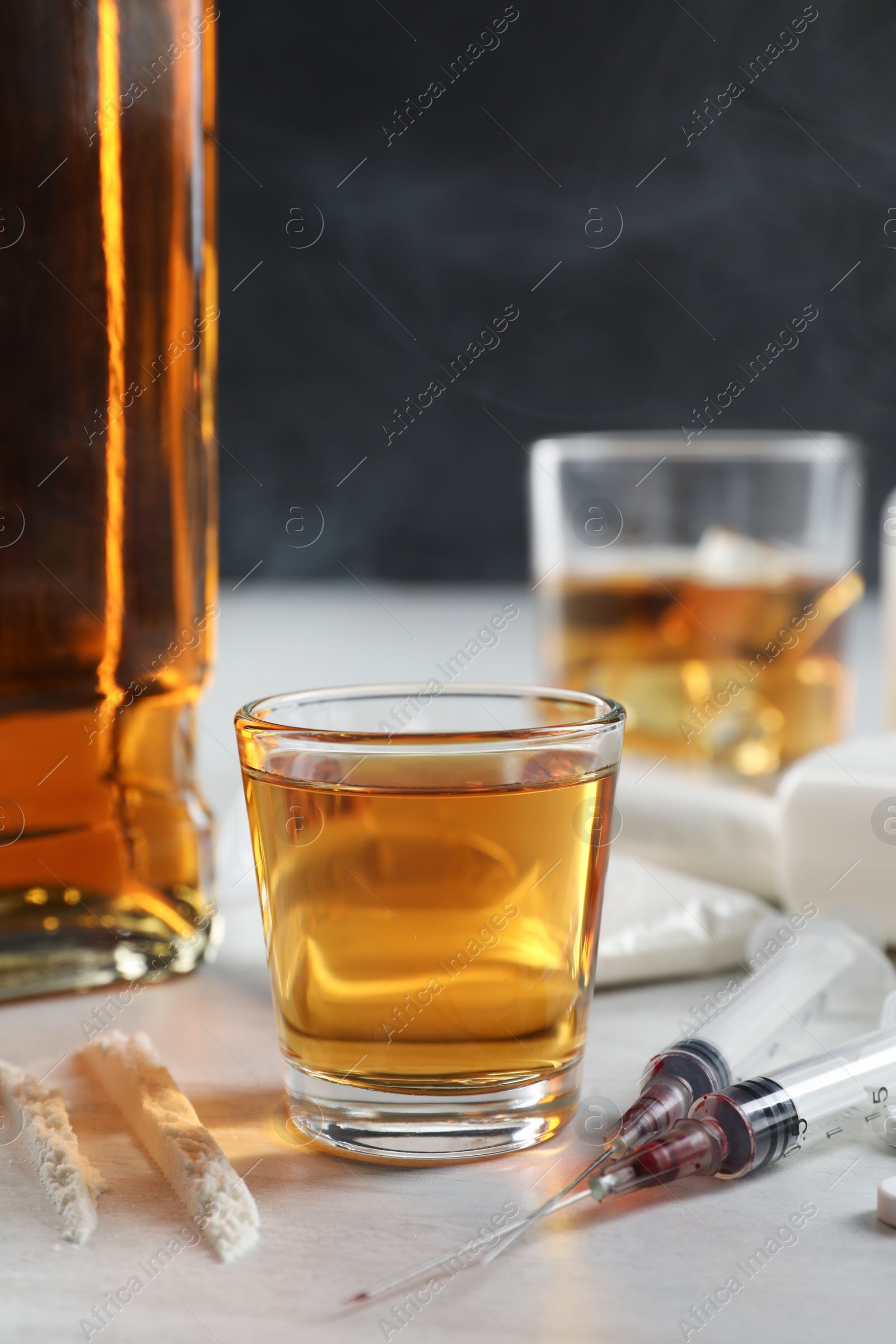 Photo of Alcohol and drug addiction. Whiskey in glass, syringes and cocaine on white table