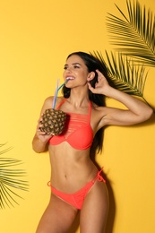 Photo of Beautiful young woman in stylish bikini with cocktail and tropical leaves on yellow background