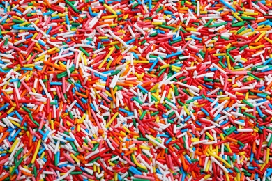 Photo of Bright colorful sprinkles as background, top view. Confectionery decor