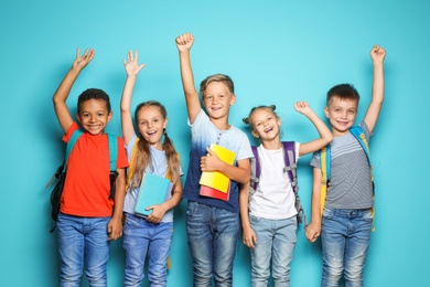 Group of little children with backpacks and school supplies on color background