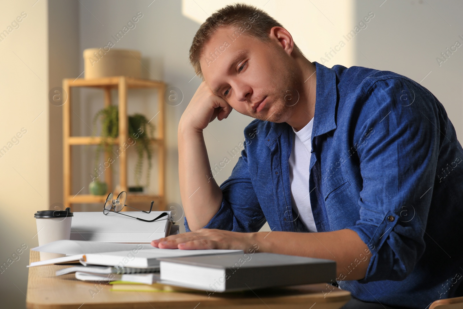 Photo of Tired man studying at wooden table indoors